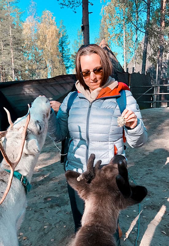 woman in silver puffer jacket feeding reindeer