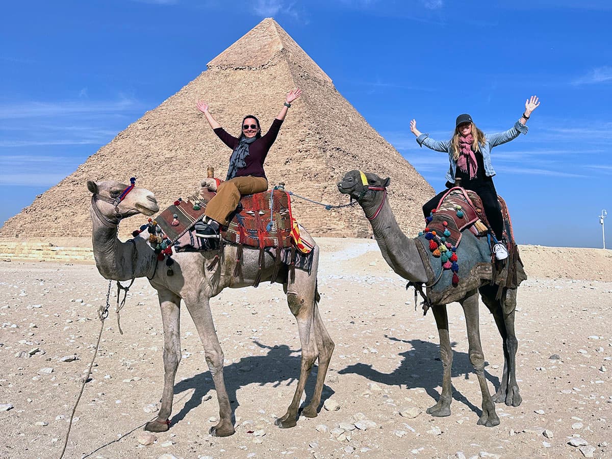 two women on camels in front of Egyptian pyramid